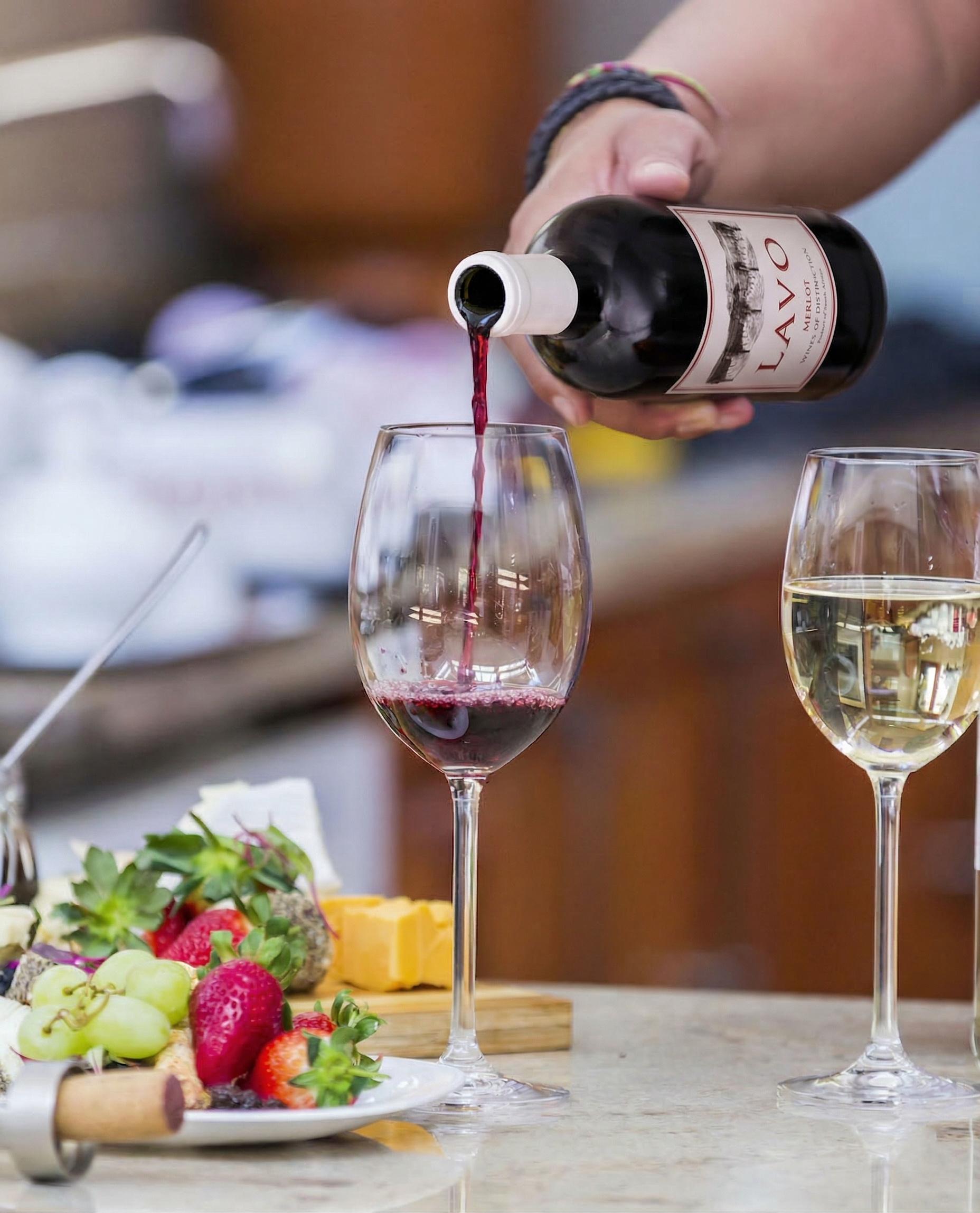 Lavo Merlot being poured into a glass alongside a fruit and cheese board